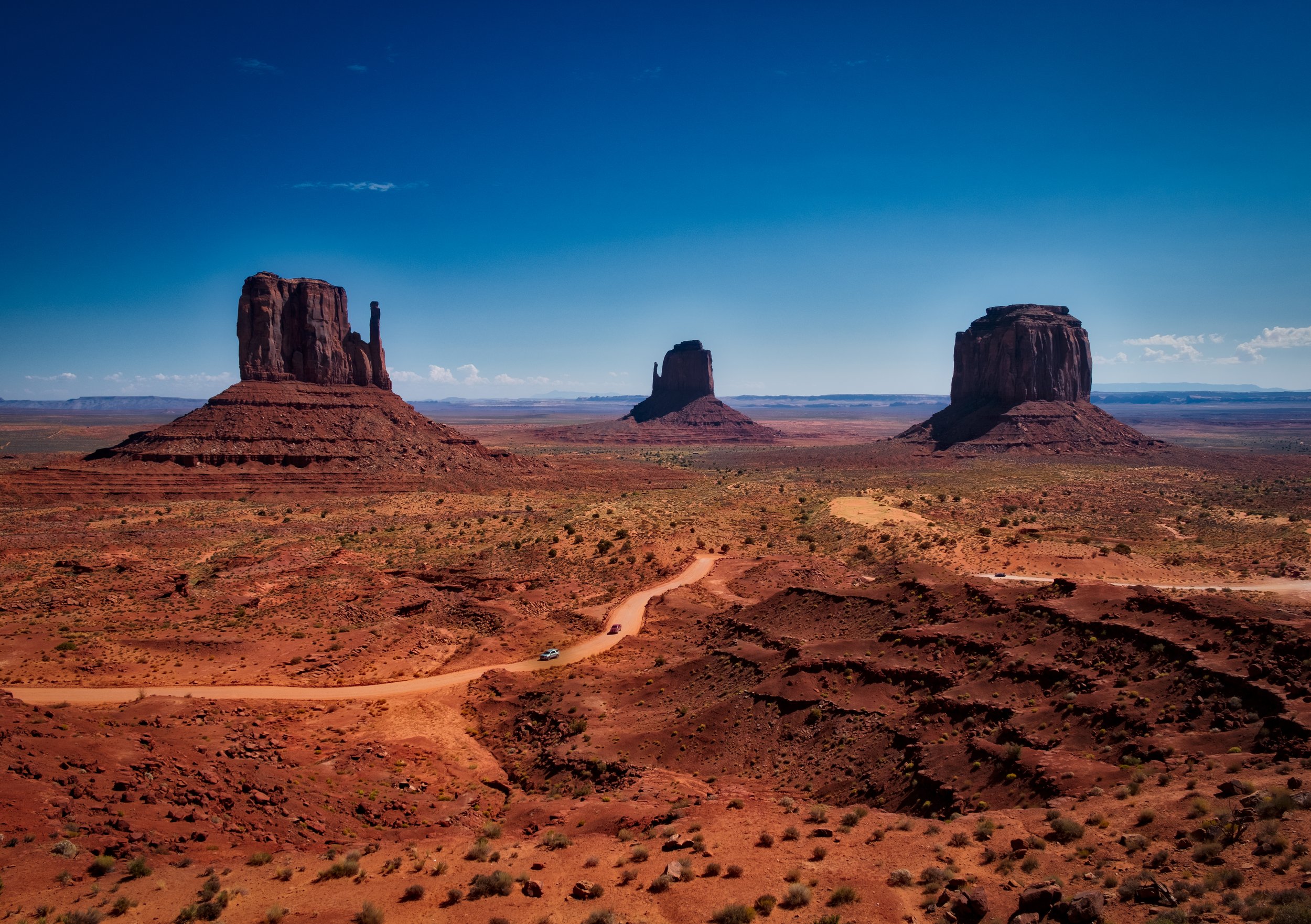 Monument Valley landscape with red rock formations and a desert road under a clear blue sky.