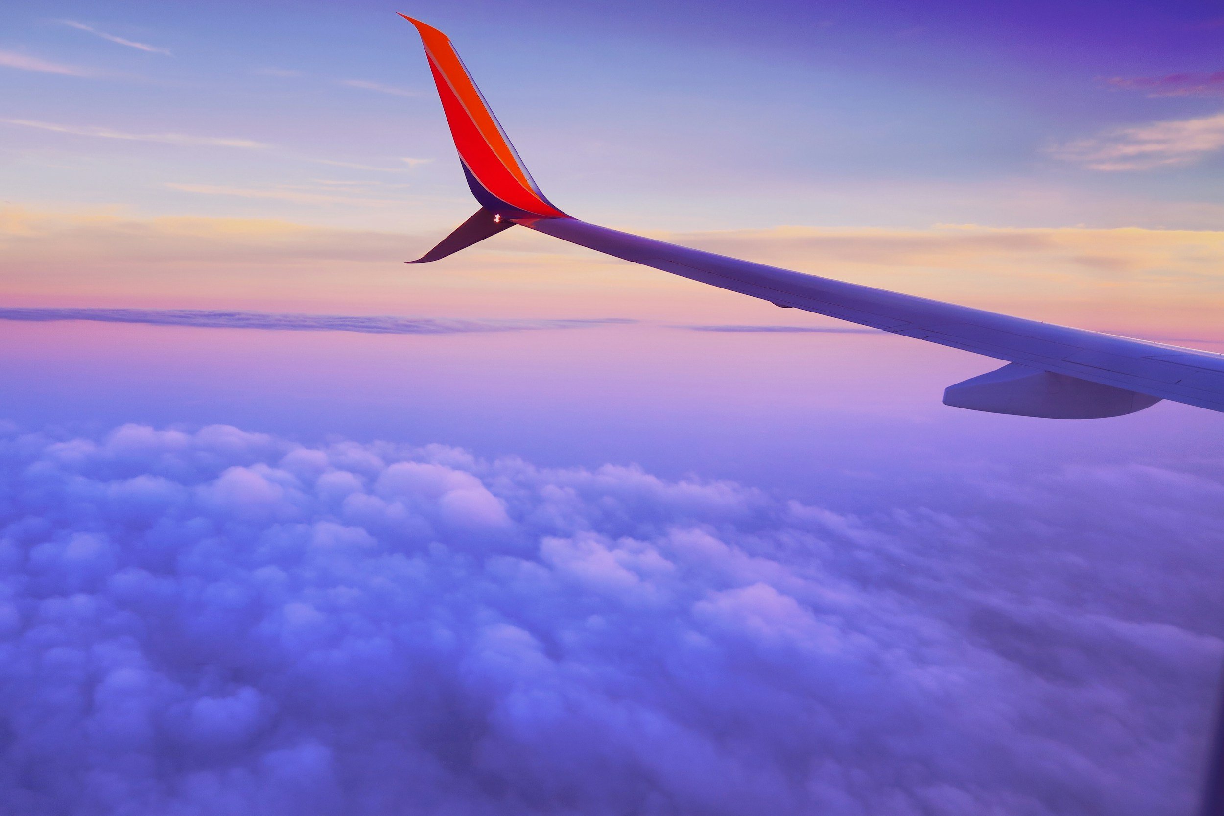 Airplane wing over clouds during sunrise or sunset - header image for SaschaGhods.com