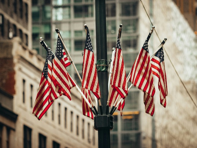 Ein Strauß amerikanischer Flaggen an einem Laternenmast zwischen Häuserfassaden.
